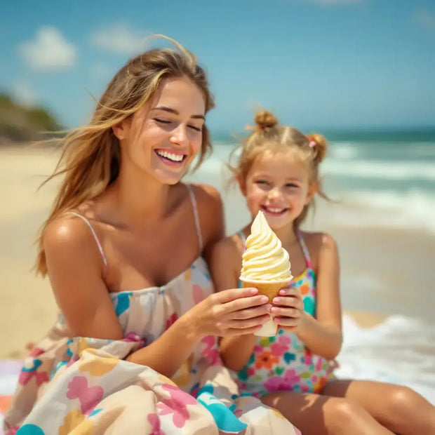 Eine Mutter und ihre kleine Tochter sitzen auf einem Strandtuch und genießen ein Softeis hellgelb mit Vanille.